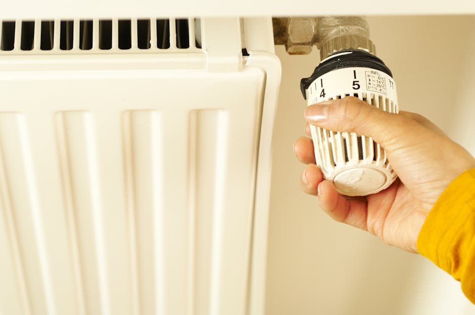 Close-up of hand adjusting radiator thermostat to control home heating temperature.